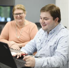 Student at laptop with faculty member smiling and assisting